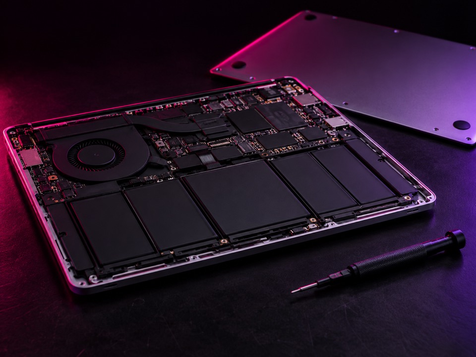 Laptop din aluminiu deschis pe masa de lucru, cu placa și bateria la vedere